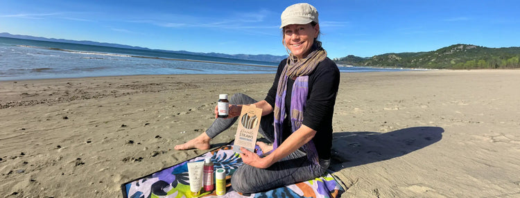 Woman sitting on a beach holding a supplement bottle and package, with a scenic background.