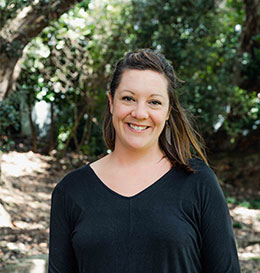 Woman wearing a black shirt standing outdoors with trees in the background