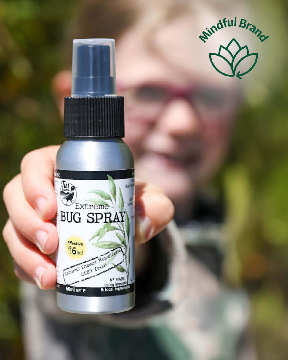 Hand holding a bottle of Extreme Bug Spray with a blurred background.