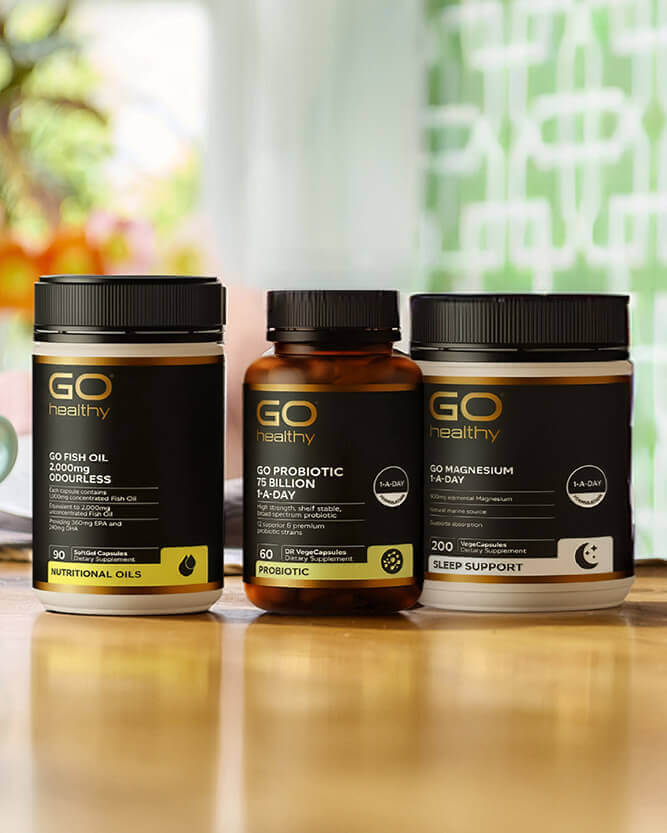 Three 'GO Healthy' supplement bottles on a wooden surface with a blurred background.