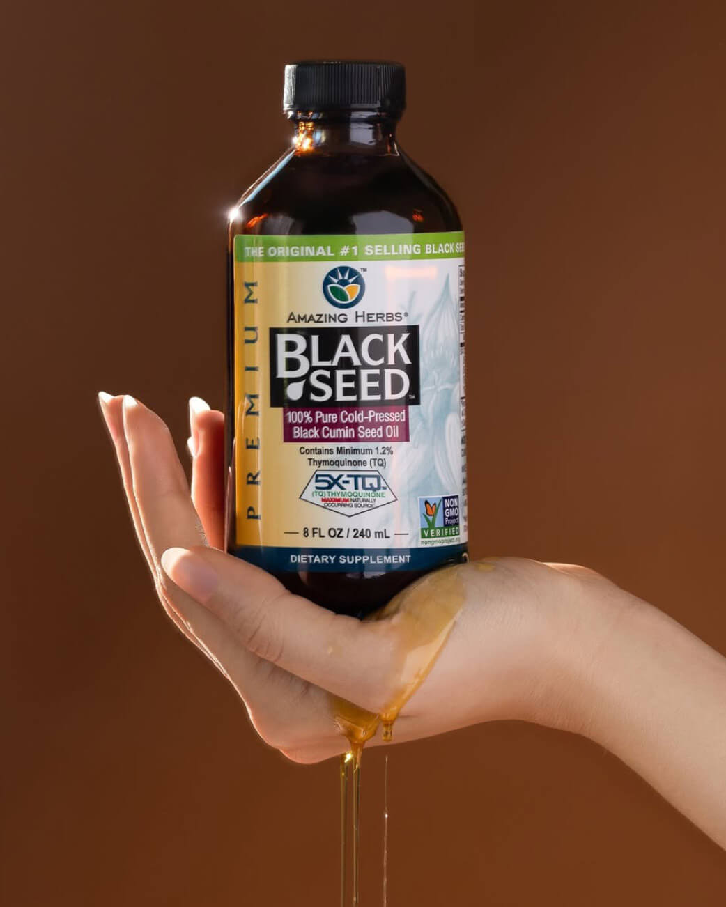 Hand holding a bottle of Amazing Herbs Black Seed oil with a brown background