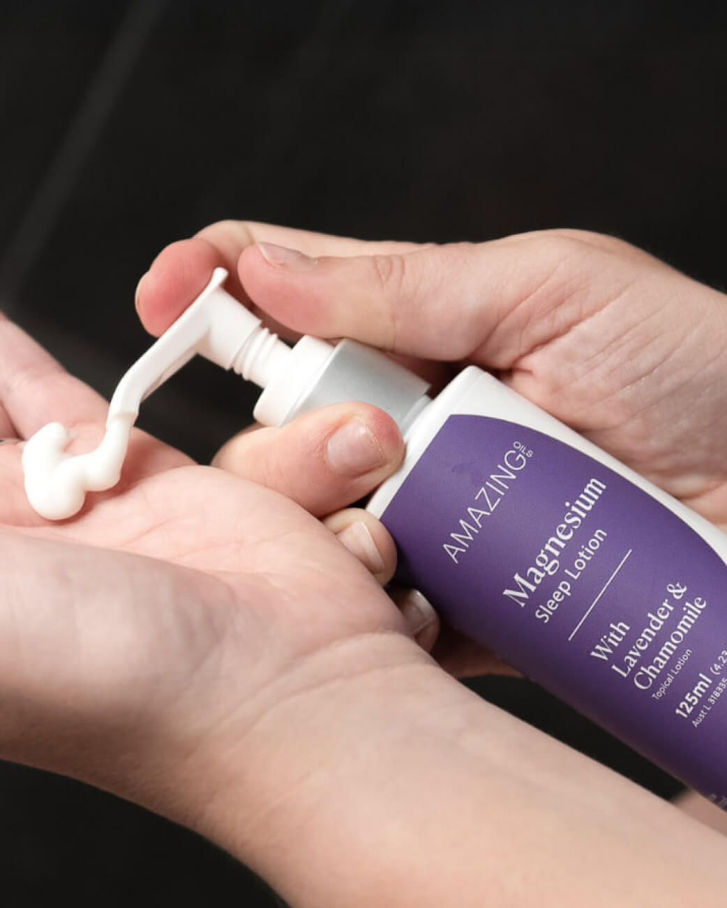 Hand holding a bottle of 'Amazing' magnesium sleep lotion with a dark background