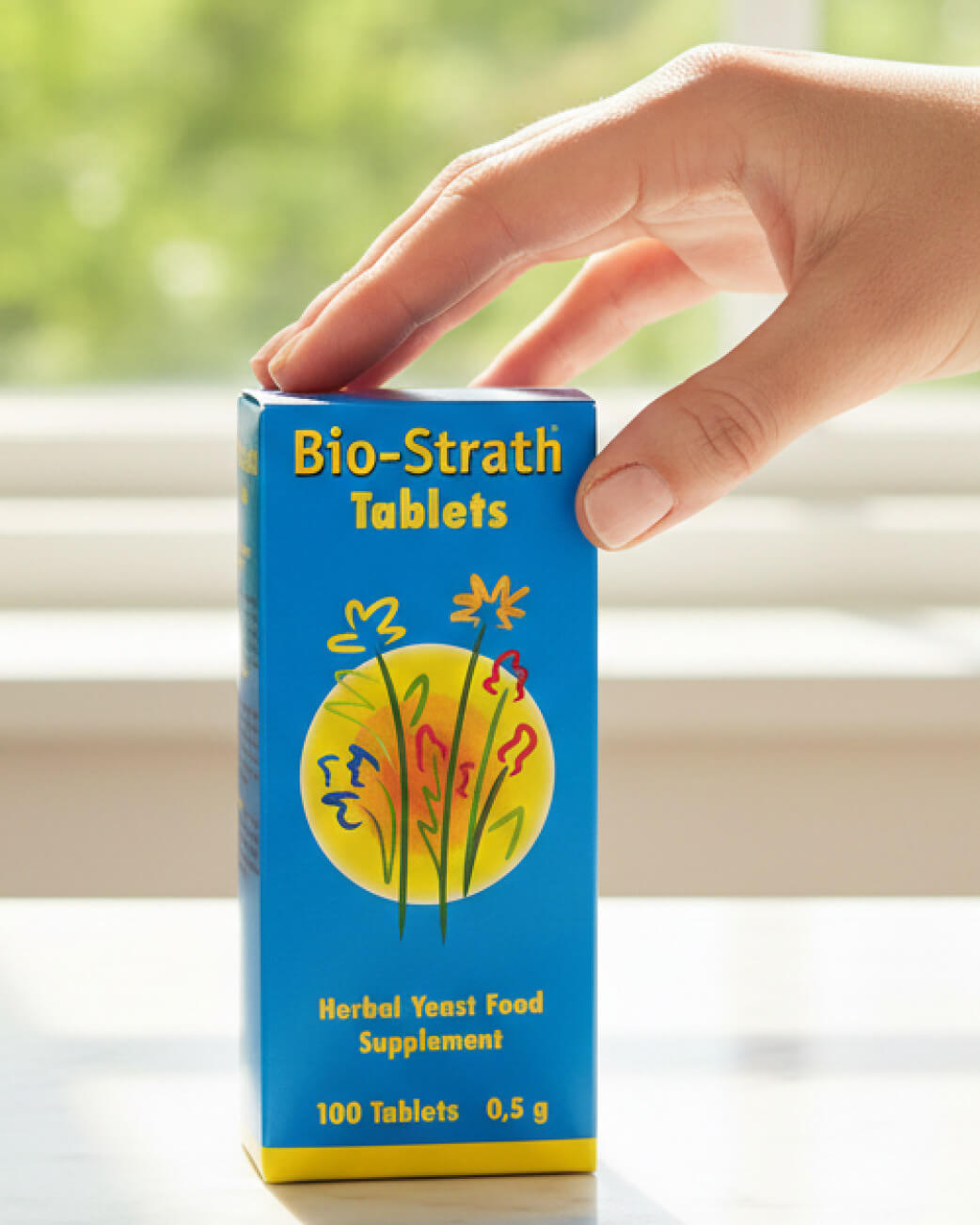 Hand reaching for a box of Bio-Strath Tablets on a table with a blurred background
