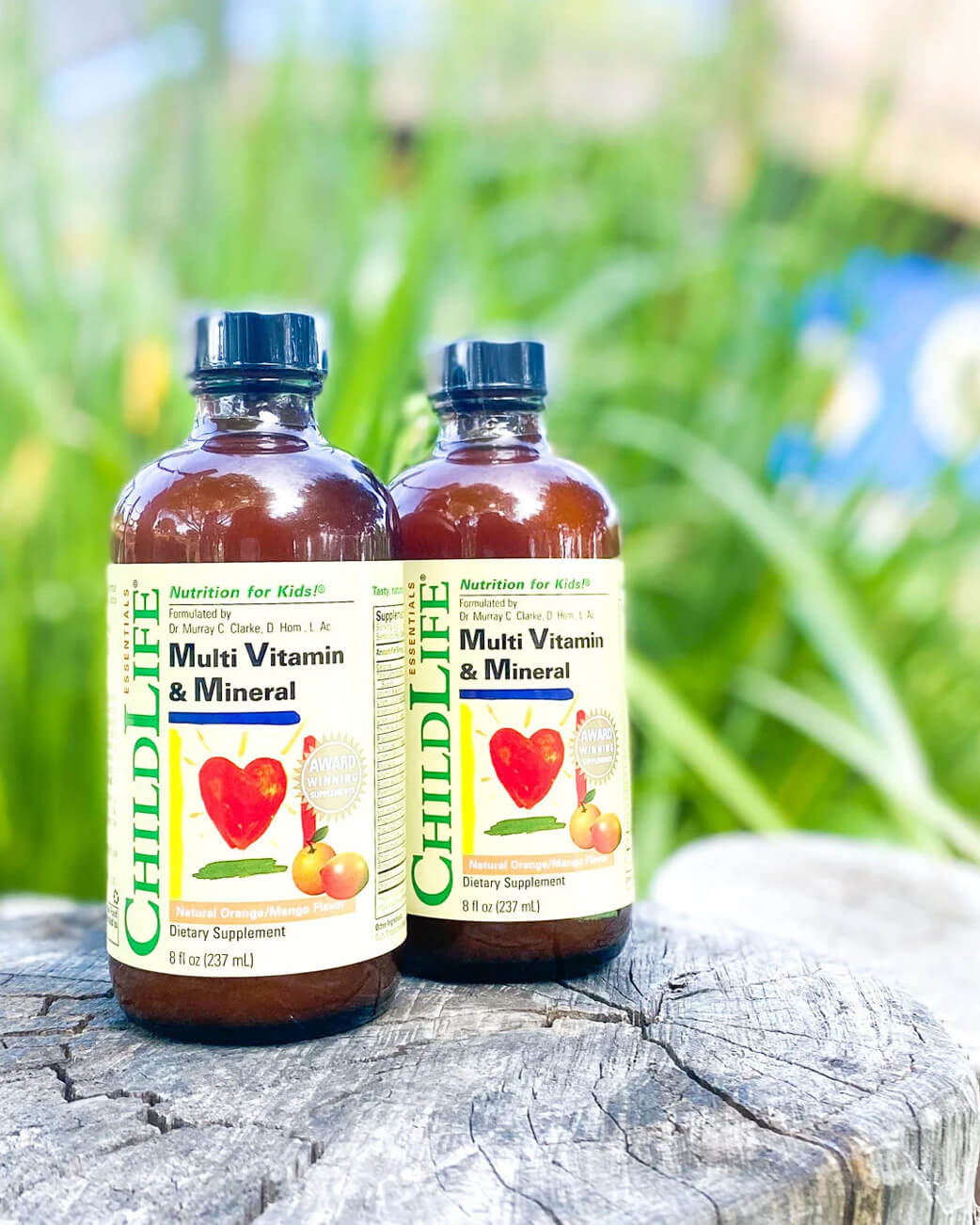 Two bottles of ChildLife Multi Vitamin & Mineral on a wooden surface with a natural background.