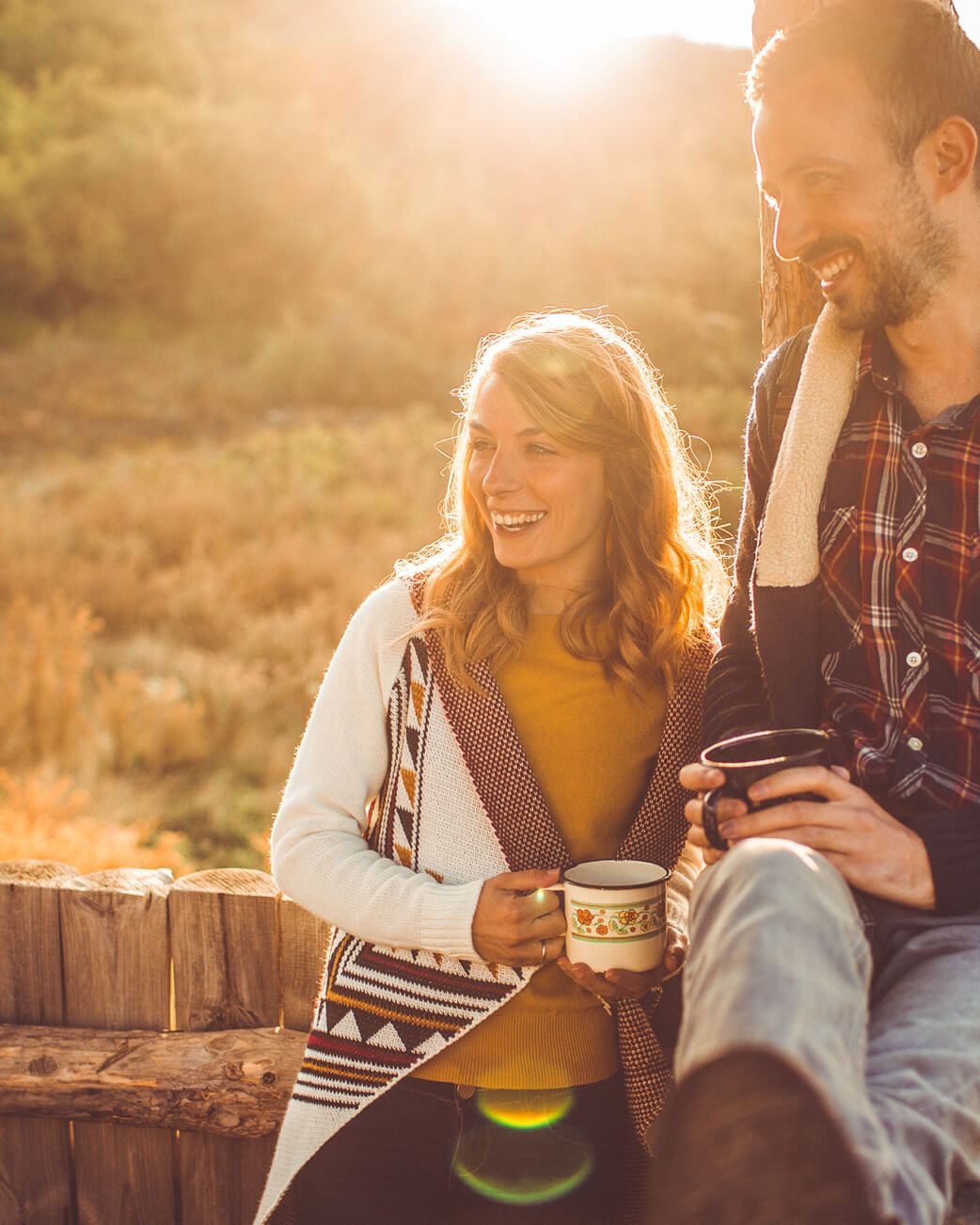 Couple sitting together outdoors with a warm glow, holding mugs.