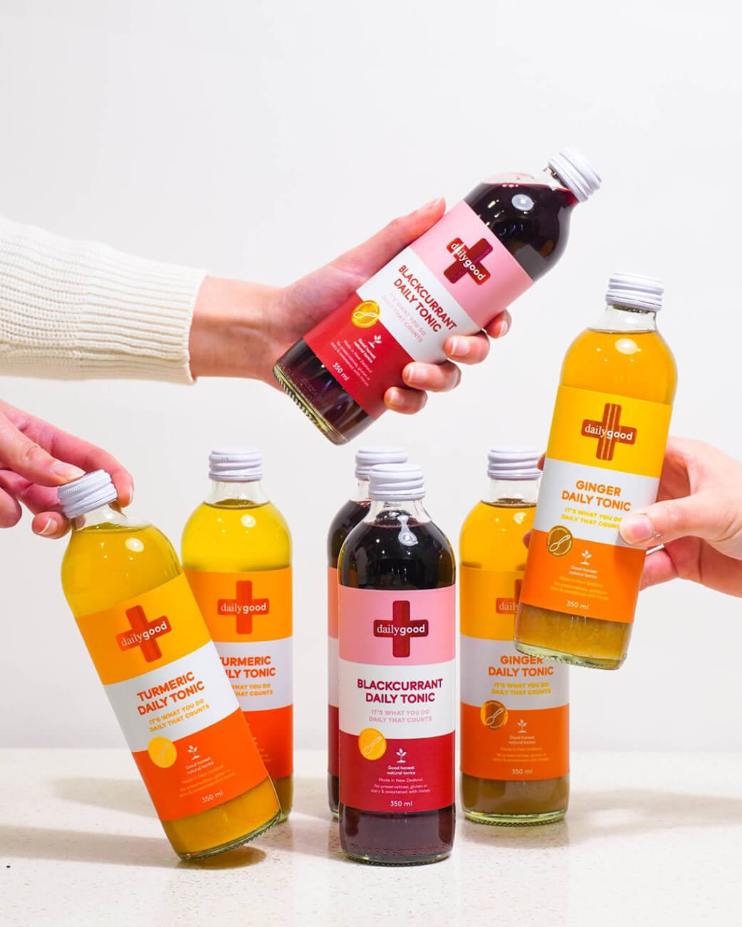 Bottles of Daily Tonics with different flavours being held by hands on a white background.