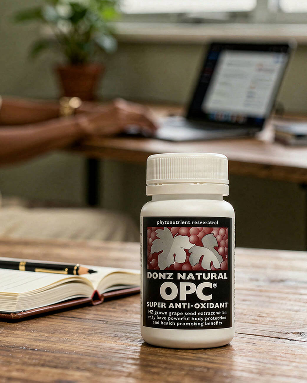 Bottle of Donz Natural OPC supplement on a desk with a laptop and notebook in the background.