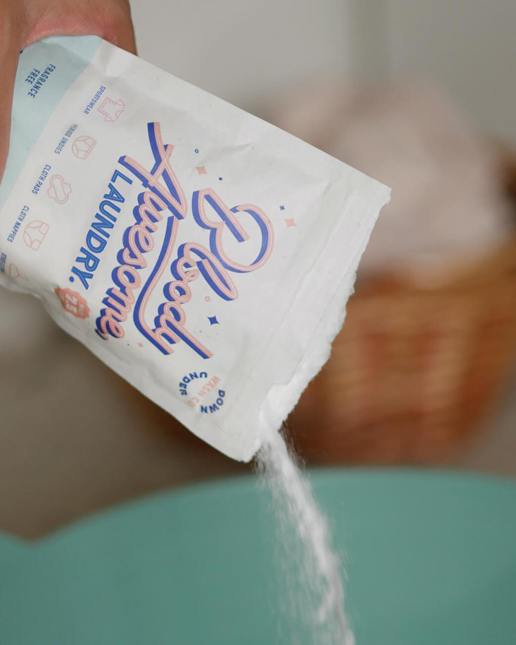 Laundry detergent being poured from a packet into a blue container.