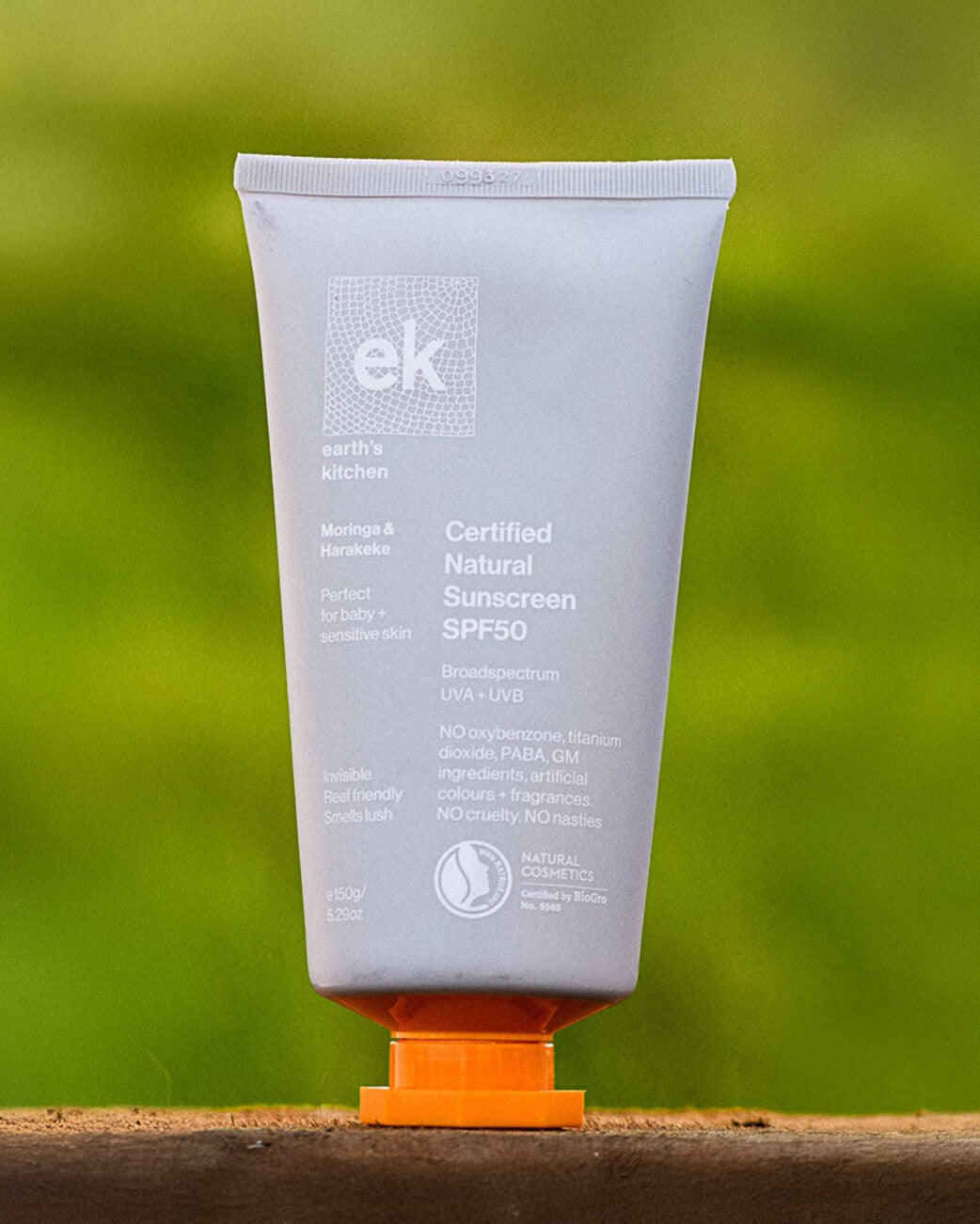 Tube of ek Certified Natural Sunscreen SPF50 on a wooden surface with a green blurred background.