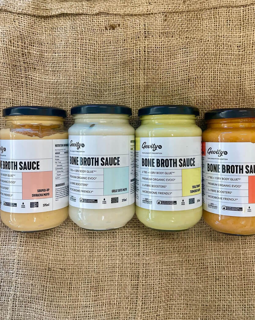 Four jars of bone broth sauce with labels on a burlap background.
