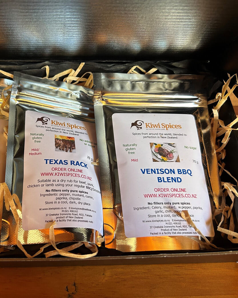 Two packages of Kiwi Spices with labels for 'Texas Rack' and 'Venison BBQ Blend' on a wooden surface.