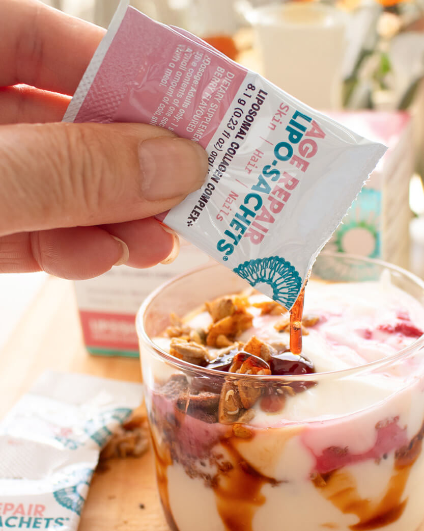 Hand holding a Lipo-Repair Sachets packet over a yogurt parfait with granola.