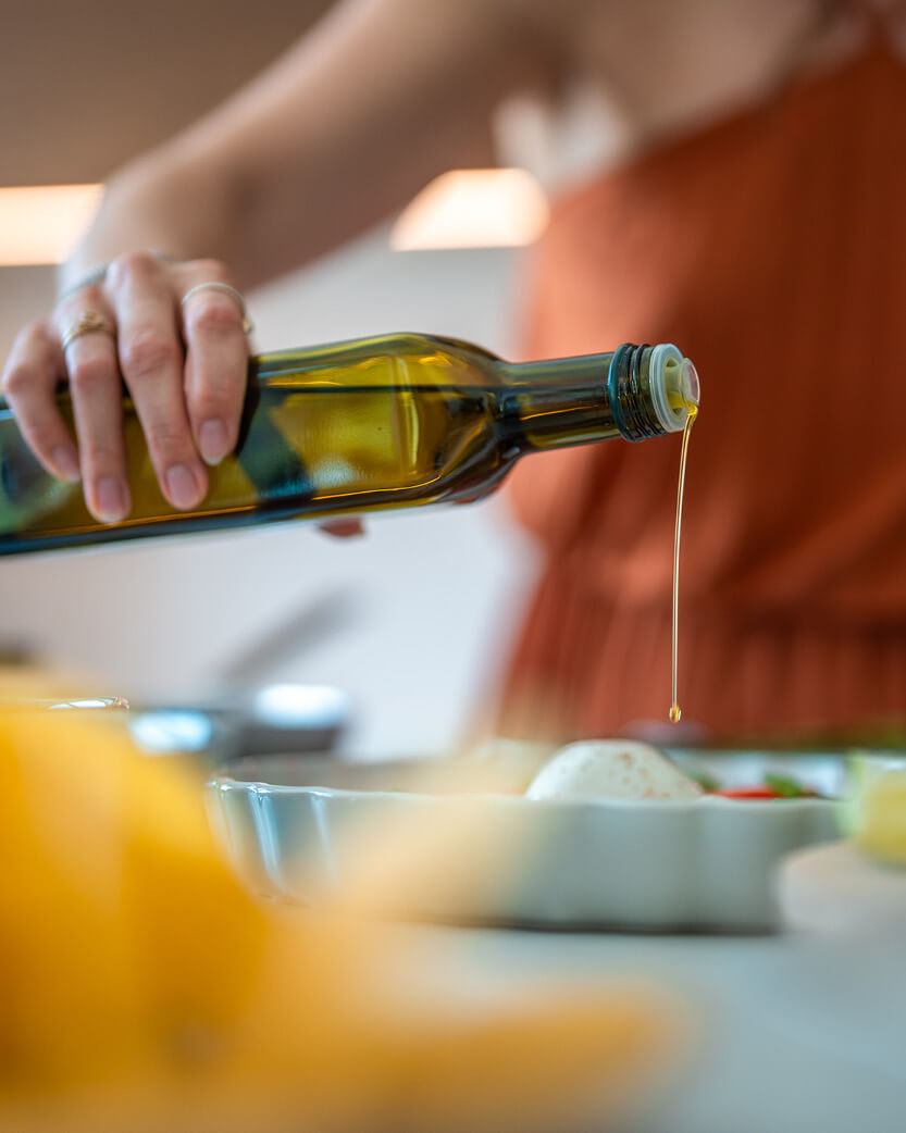 Person pouring olive oil from a bottle into a dish on a kitchen counter.