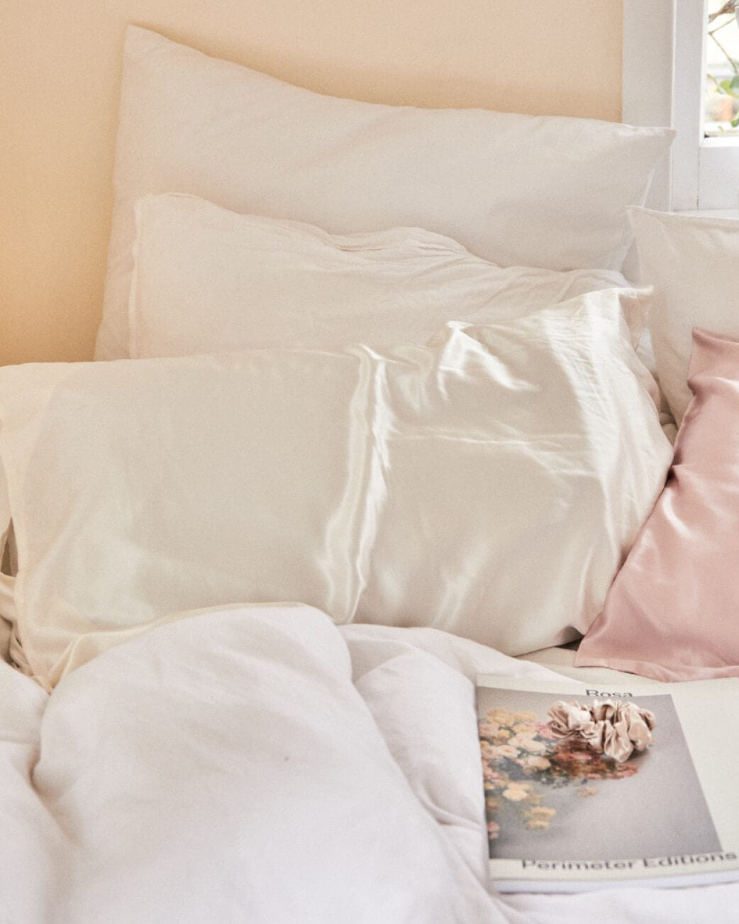 Neatly made bed with white and pink pillows and a magazine on a nightstand.