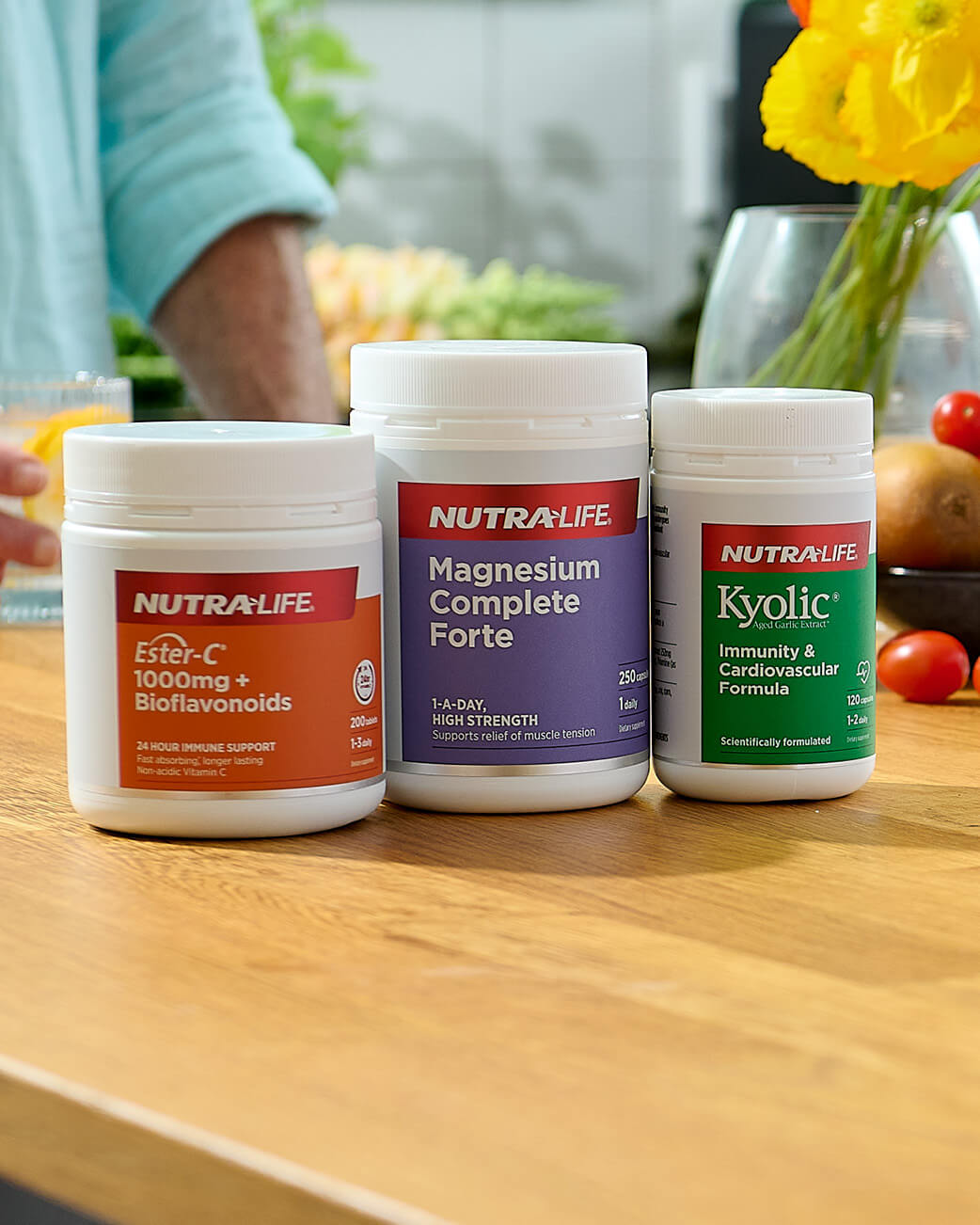 Three NutraLife supplement containers on a wooden table with a blurred background of a kitchen.