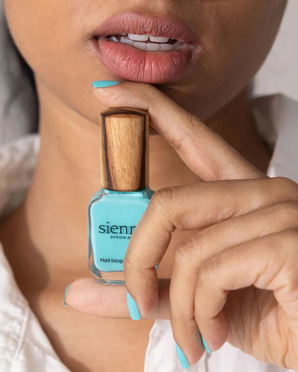 Person holding a bottle of turquoise nail polish with wooden cap.