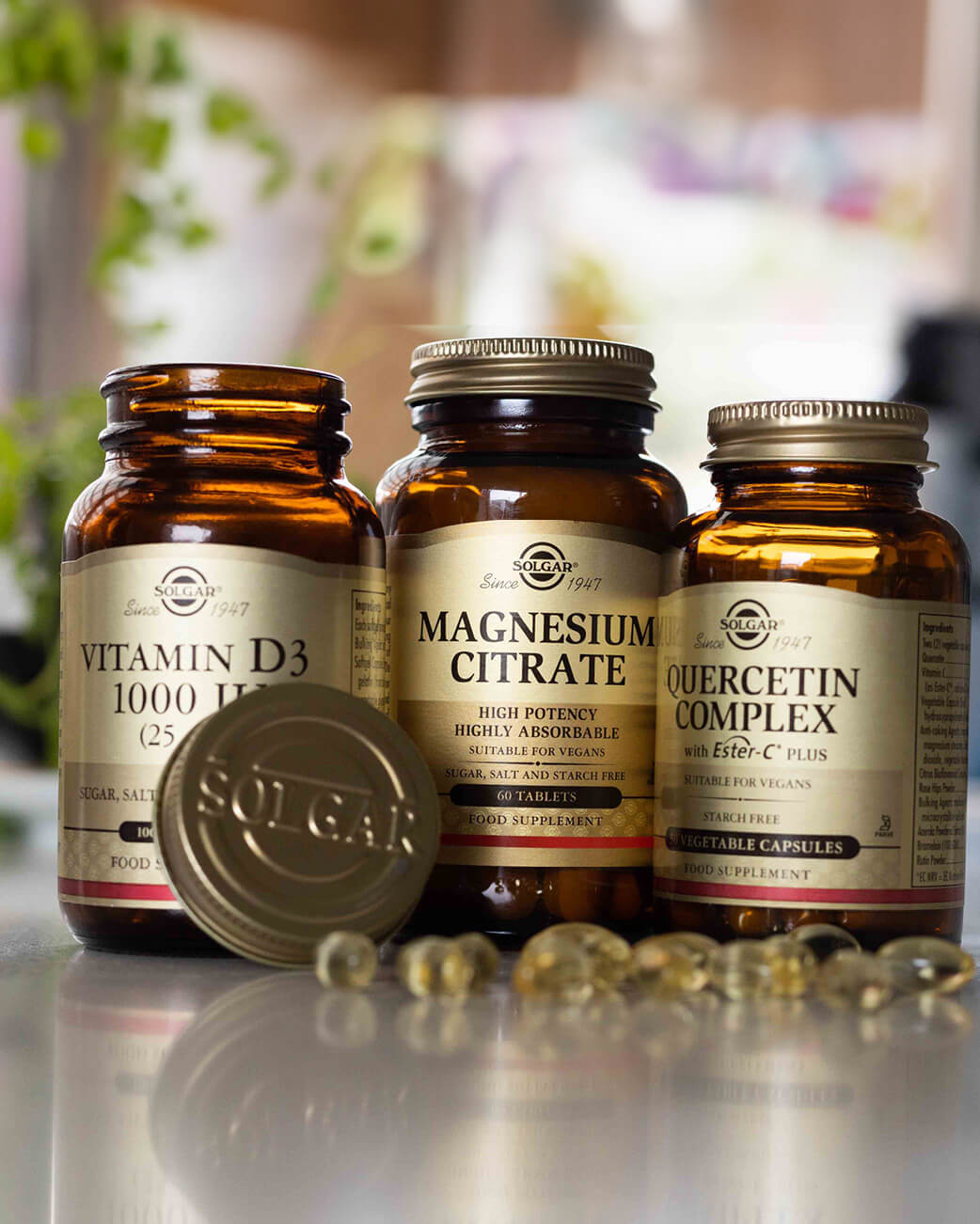 Three supplement bottles labeled Vitamin D3, Magnesium Citrate, and Quercetin Complex on a reflective surface with a blurred natural background.