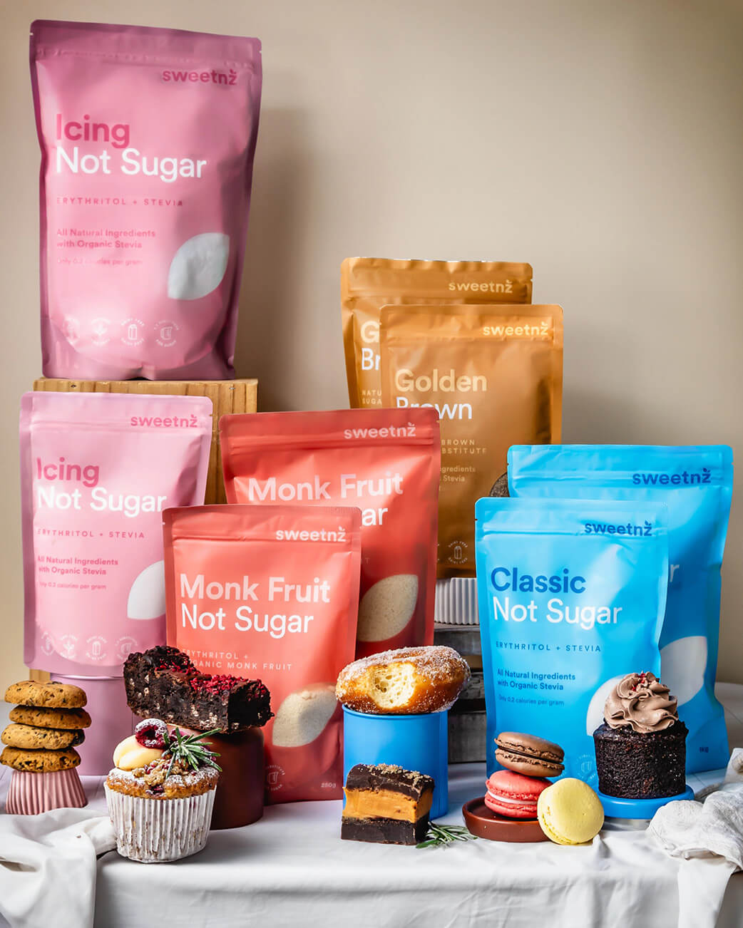 Assorted sweetener packages including pink, orange, and blue bags on a neutral background with small desserts.
