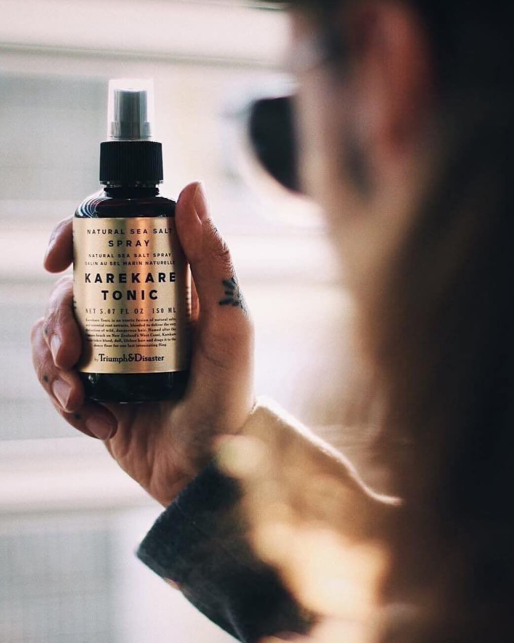 Person holding a bottle of Karekare Tonic spray with a blurred background.