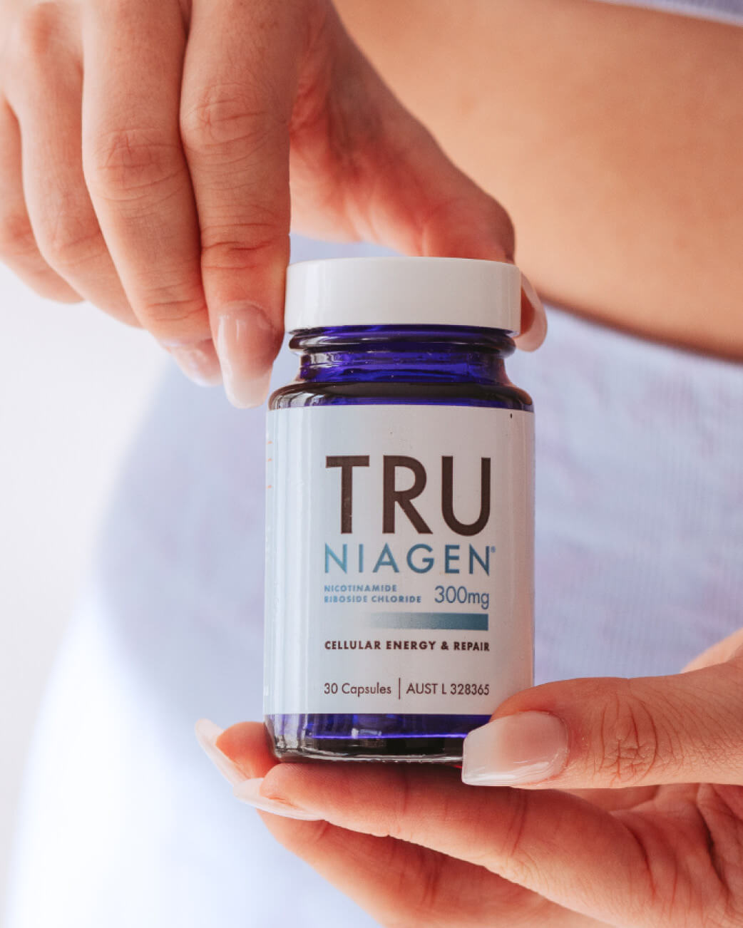 Hand holding a bottle of Tru Niagen supplement with a white background.