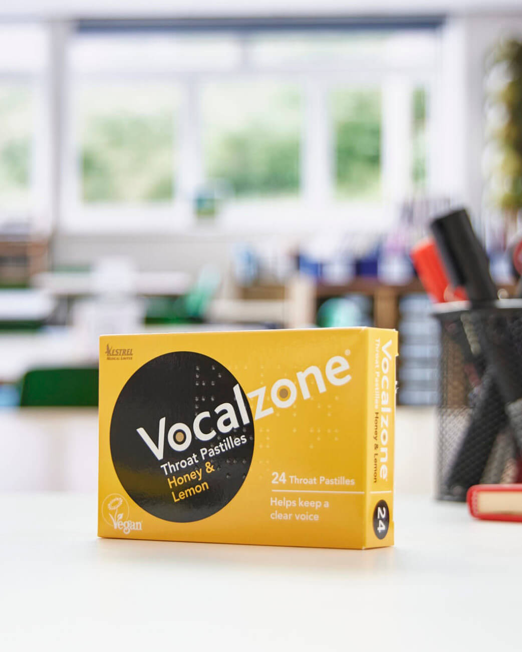 Vocalzone throat pastilles box on a desk with a classroom background.