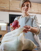 Woman in a kitchen holding an apple and a reusable mesh bag.