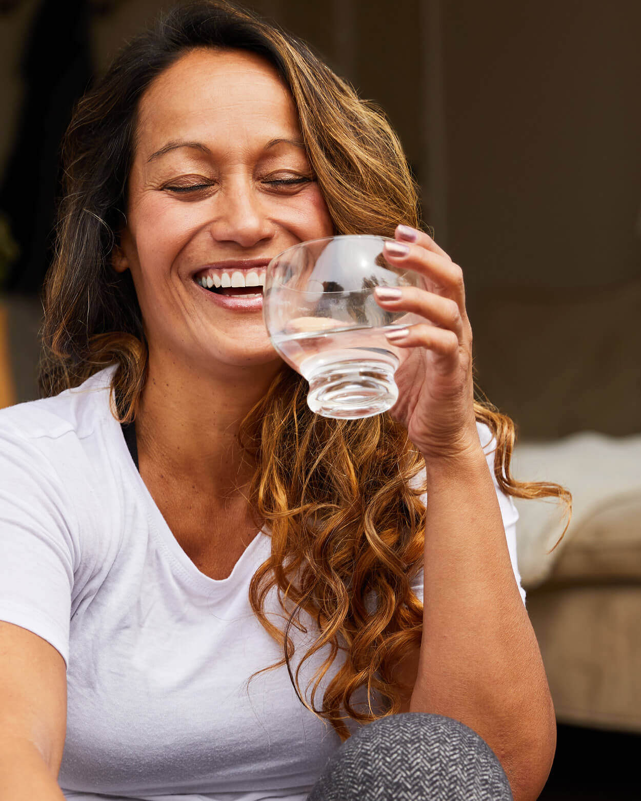Woman holding a glass of water and smiling outdoors.