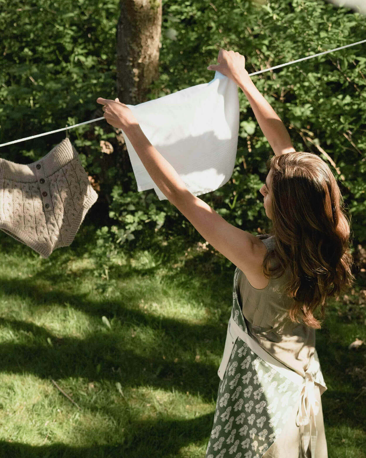 Woman hanging clothes on a line in a garden.