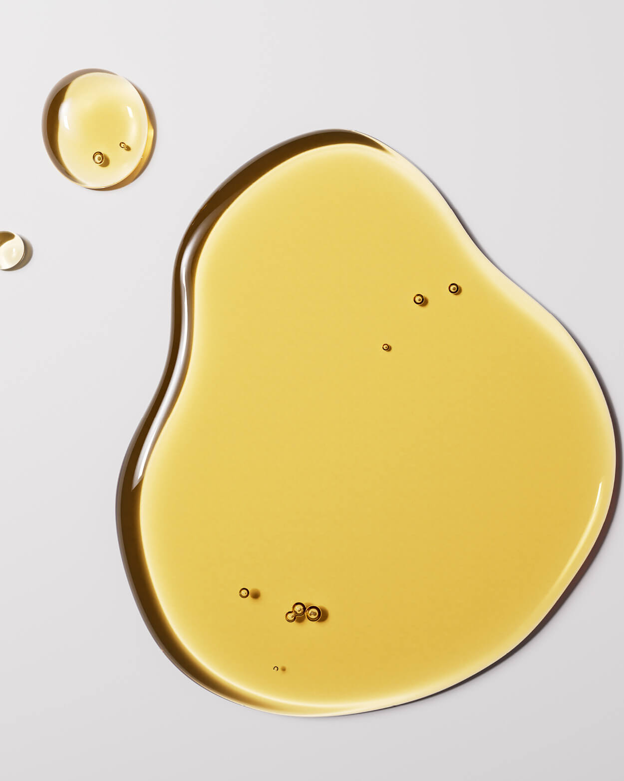 Yellow oil droplet and pool on a light grey background.