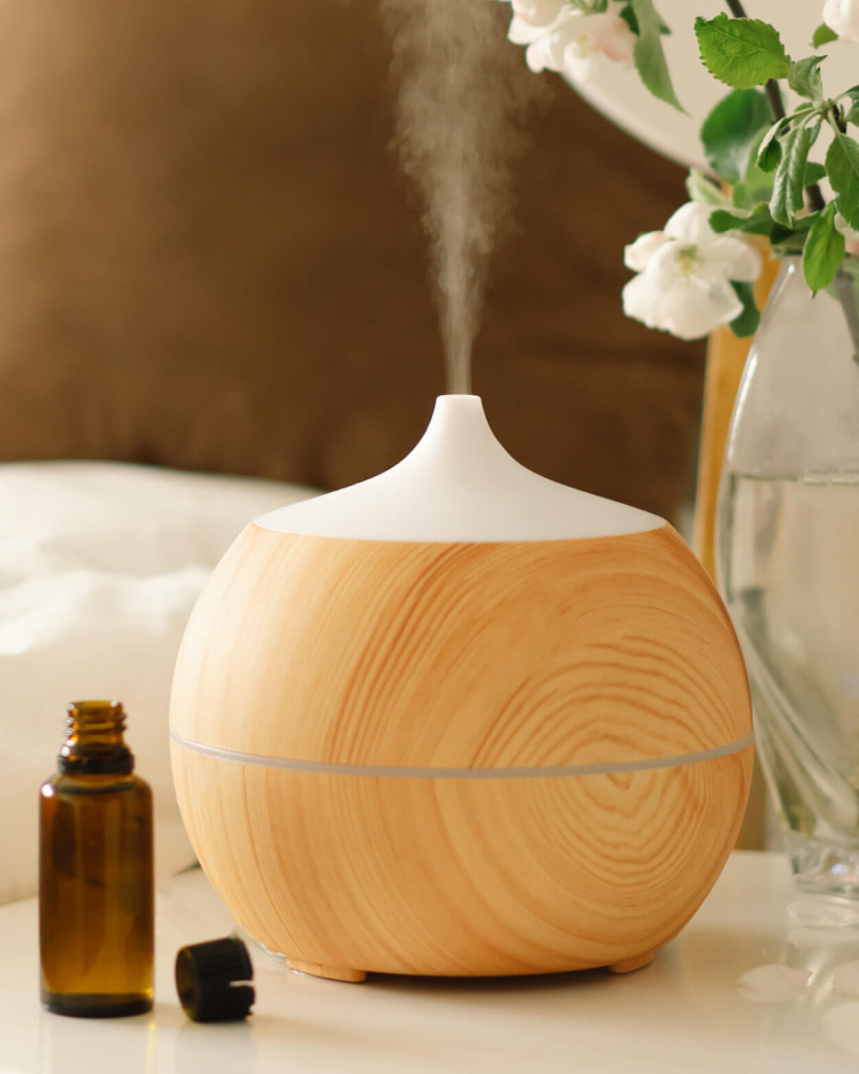 Wooden diffuser with steam, bottle, and flowers on a surface.