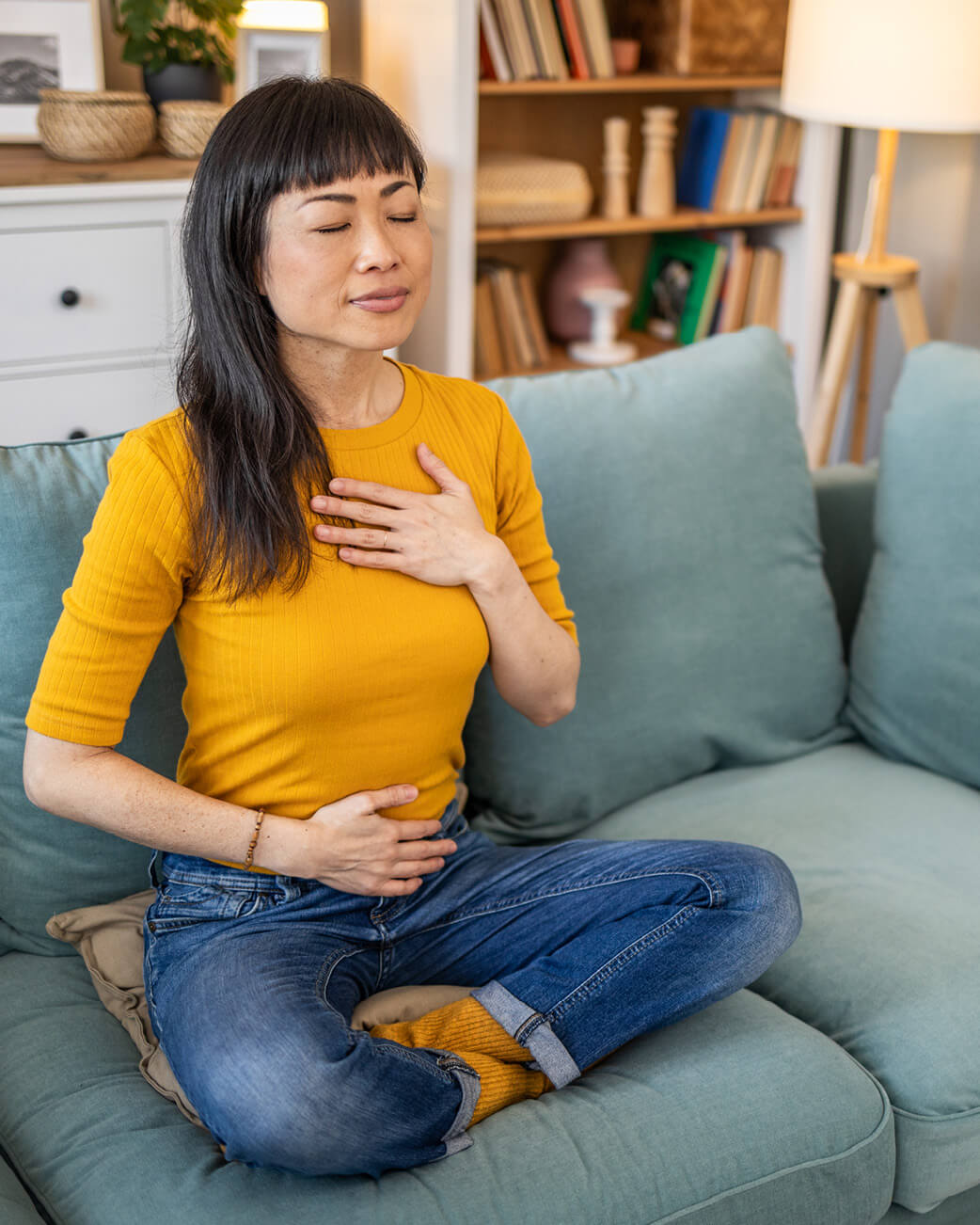 Woman sitting on a couch with her hand on her chest, possibly experiencing discomfort.