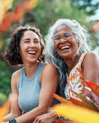 Two women laughing together outdoors with a blurred natural background