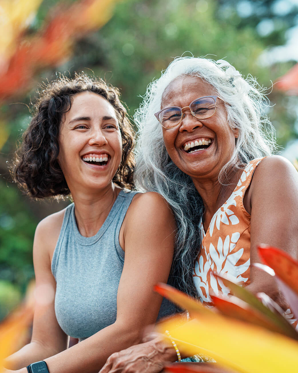 Two women laughing together outdoors with a blurred natural background