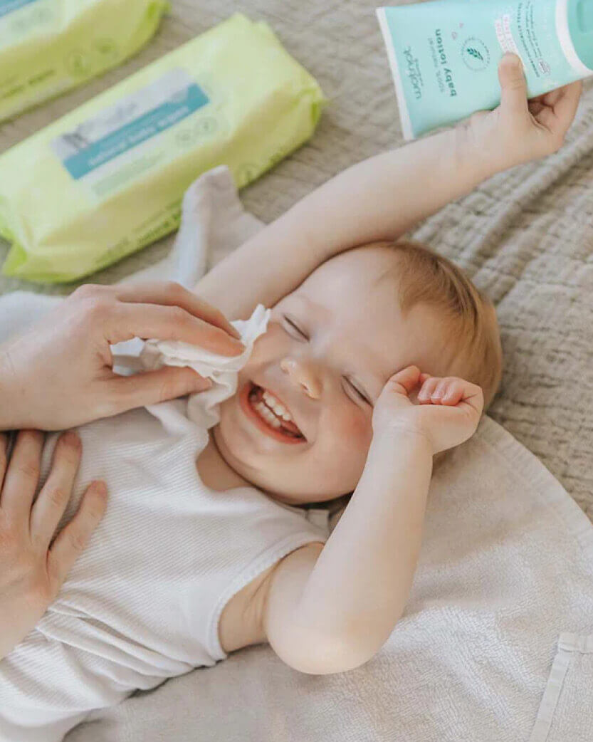 Baby lying on a blanket with a tissue and a bottle of baby lotion in the background.