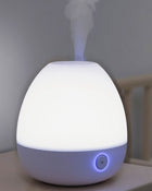 White humidifier emitting mist on a blurred background.
