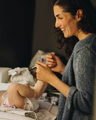 Woman in a gray sweater holding a baby in a cozy indoor setting.