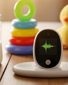 Baby monitor with screen displaying sound waves on a wooden surface with colorful toys in the background.