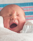 Newborn baby with a striped blanket in the background.