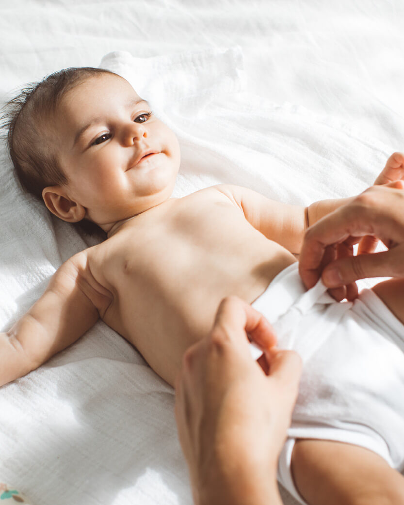 Baby lying on a white blanket with a person's hand holding their foot.