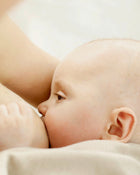Close-up of a baby being held by an adult, with a neutral background.
