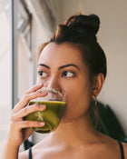 Woman drinking a green smoothie indoors.