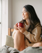Woman holding a red mug, sitting on a couch by a window.
