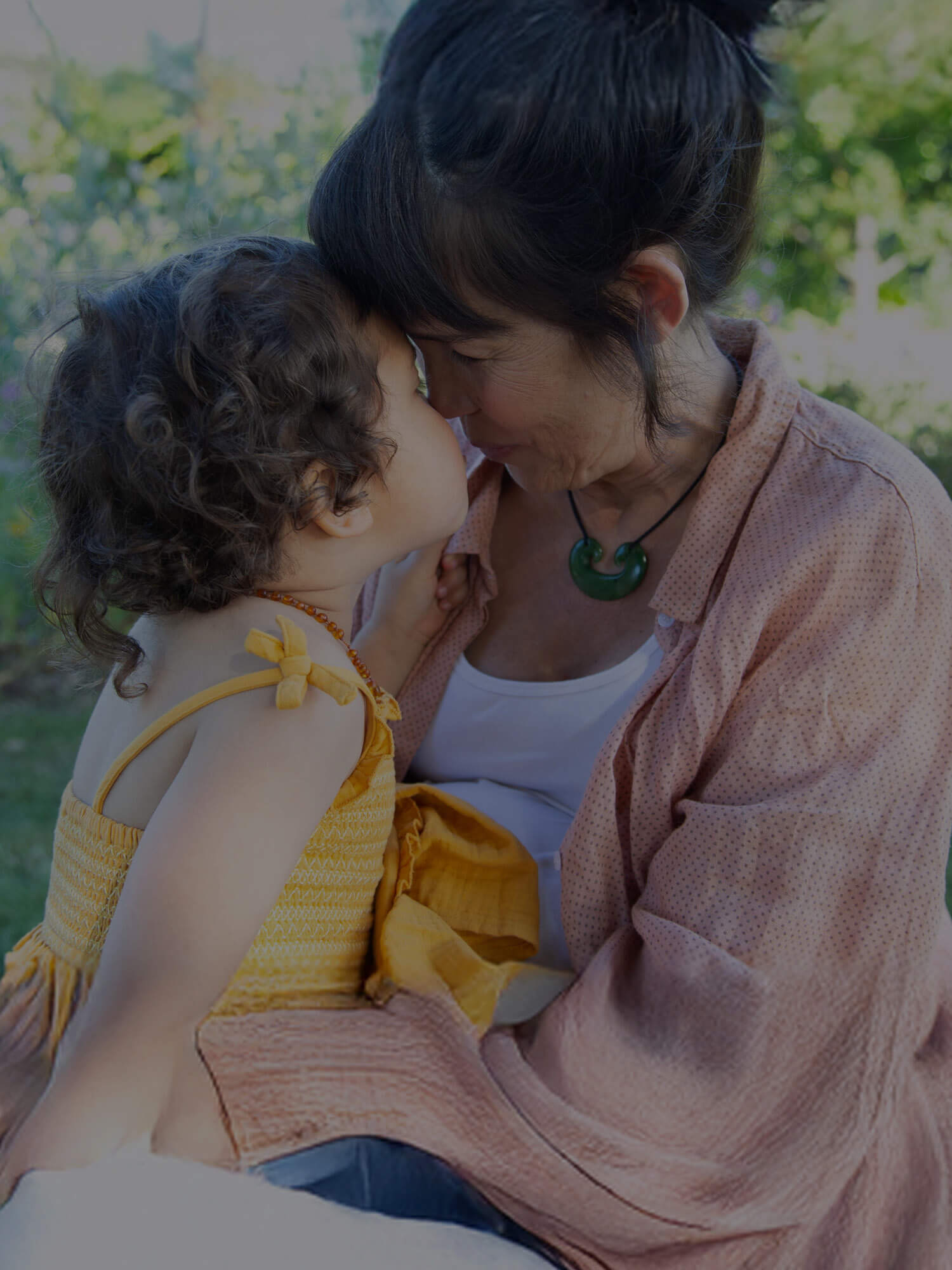 Woman and child sitting together outdoors with a blurred background.
