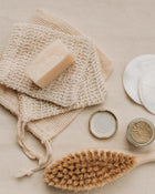 Natural skincare products including a soap bar, loofah, brush, and jars on a neutral background.