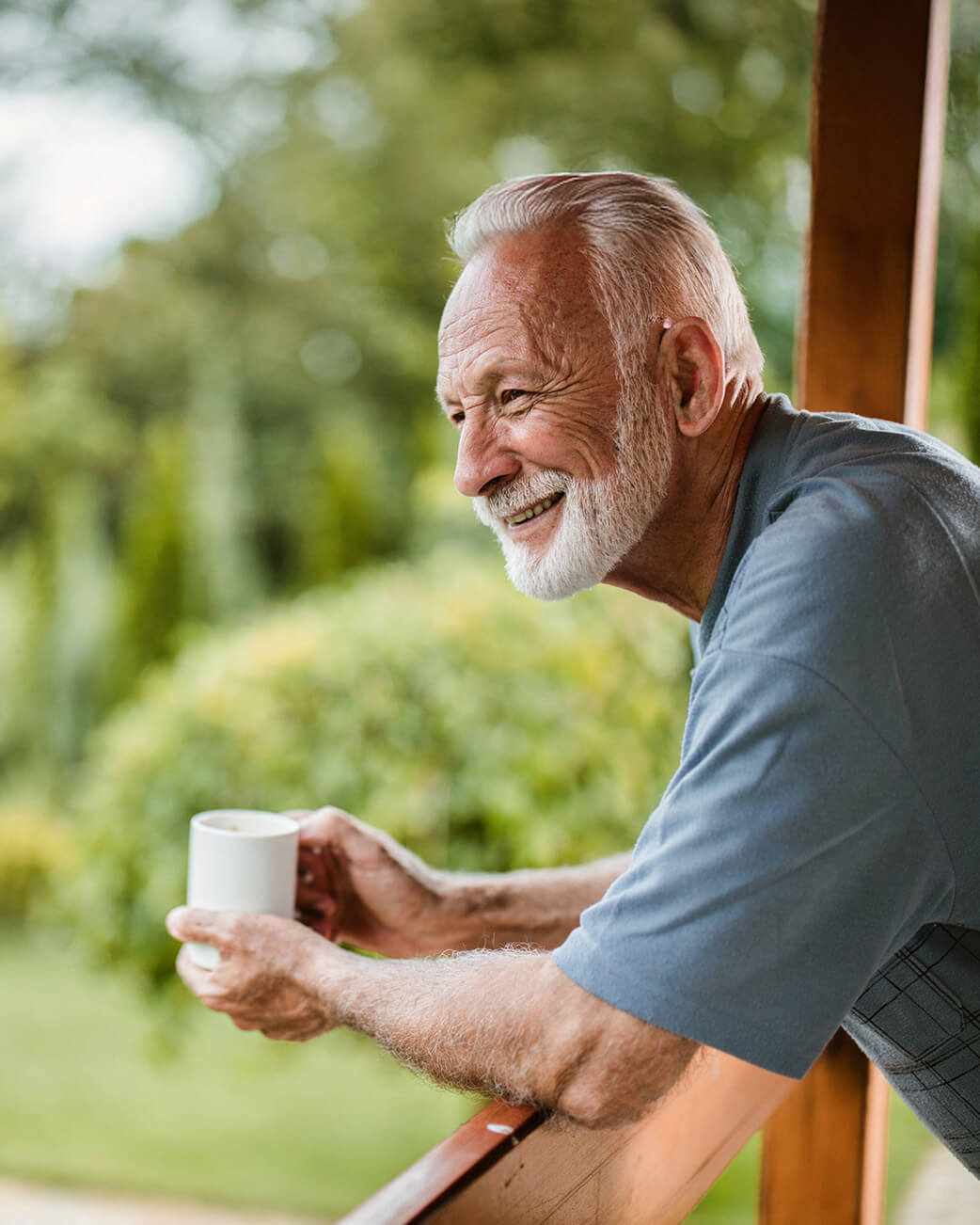 Man with a beard holding a mug outdoors, smiling.