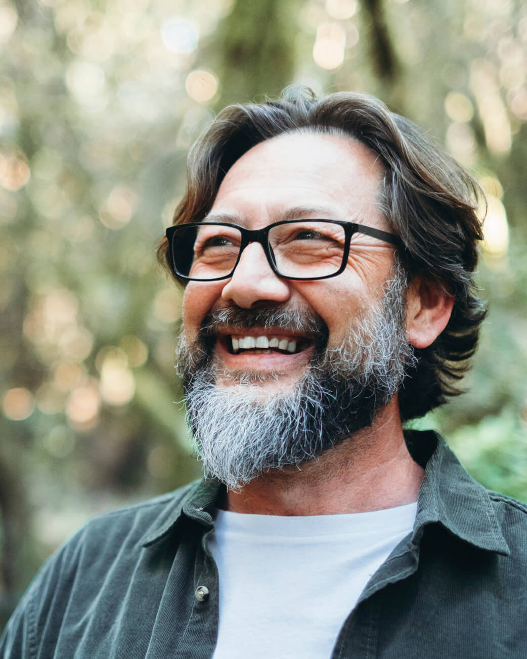 Man with glasses and a beard smiling outdoors.
