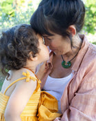 Woman and child embracing outdoors with greenery in the background.