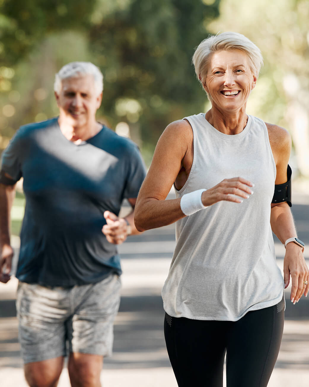 Two elderly individuals jogging outdoors on a sunny day.