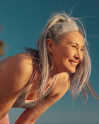 Woman with grey hair smiling outdoors against a clear blue sky.