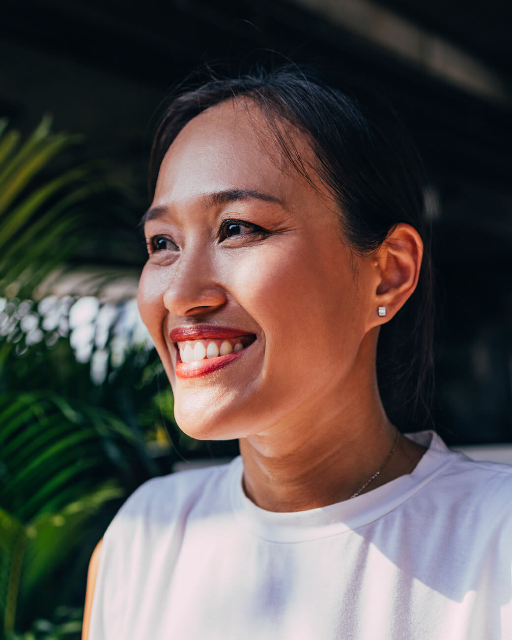Woman smiling outdoors with greenery in the background.